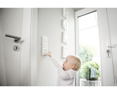 Copil care încearcă să atingă o priză cu protecție pentru copii