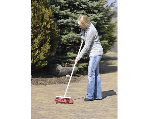 Femeie mătură o suprafață pavată în grădină cu o mătură de stradă.