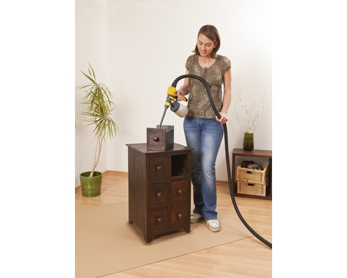 Femeie folosind pistol de pulverizare vopsea pe un dulap mic de lemn într-o cameră.