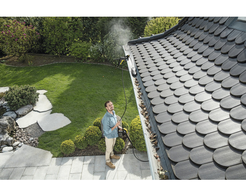 Un bărbat curăță o jgheab cu un curățător cu presiune înaltă într-o grădină.