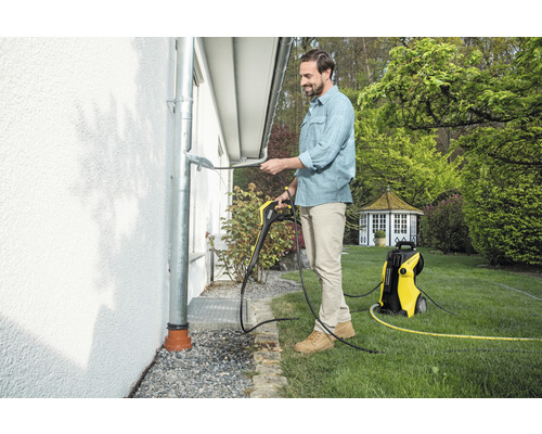 Un bărbat curăță o jgheab cu un aparat de curățat cu presiune Kärcher în grădină.