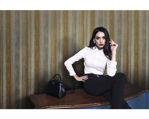 Femeie așezată pe un dulap în fața unui tapet cu dungi