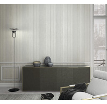 Cameră de zi cu lampă de podea, comodă și fotoliu în fața unui tapet cu dungi