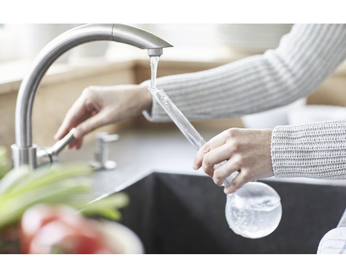 Femeie umplând o sticlă de sticlă cu apă de la robinet