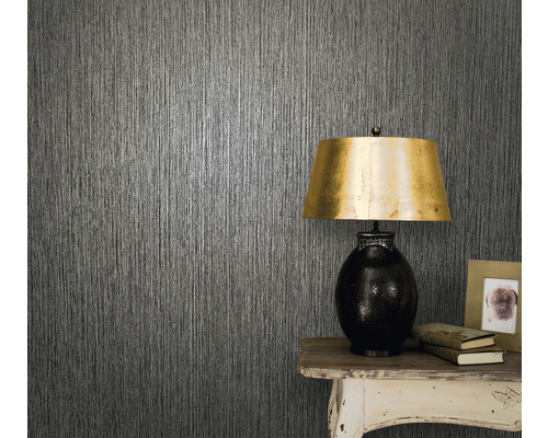 Prim-plan al unui perete cu tapet texturat, o masă și o lampă de masă.