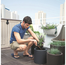 Un bărbat plantează un ghiveci împletit pe o terasă pe acoperiș cu o jardinieră, o cutie de depozitare și scânduri de terasă