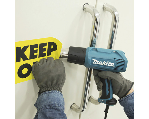 O persoană folosește un pistol cu aer cald marca Makita pentru a îndepărta un semn cu inscripția „Keep Off”.