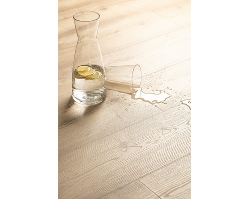 Scenă decorativă cu o carafă cu apă cu felii de lămâie și un pahar răsturnat pe o podea de lemn deschisă la culoare