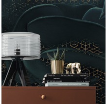 Scenă decorativă cu lampă, plantă, figurină decorativă și cărți pe o comodă în fața unui tapet cu model