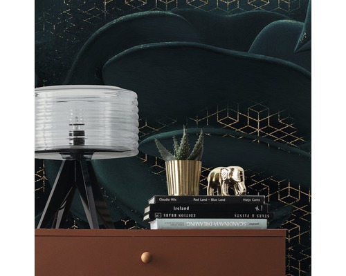 Scenă decorativă cu lampă, plantă, figurină decorativă și cărți pe o comodă în fața unui tapet cu model