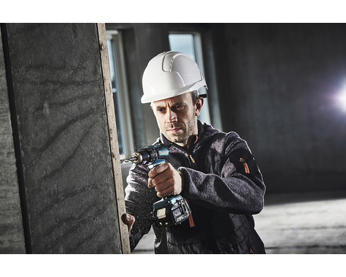 Un bărbat cu cască de protecție găurește o piesă de lucru cu o mașină de găurit cu acumulator