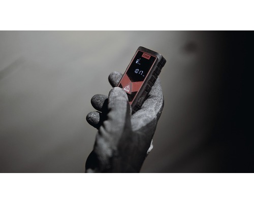 O mână cu mănușă de lucru ținând un telemetru laser.