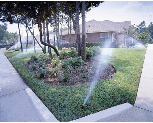 Sistem de irigare pentru un gazon și o zonă de grădină în fața unei case de locuit.