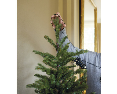 O persoană decorează un pom de Crăciun cu un șir de lumini.