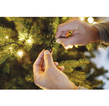 O persoană fixează un șir de lumini de un brad de Crăciun cu cleme de fixare.