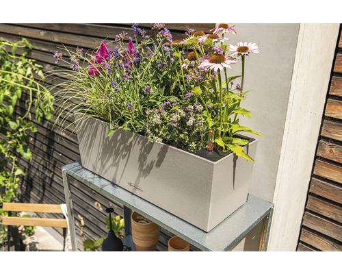 Jardinieră bej cu diverse plante pe un cadru metalic în grădină.