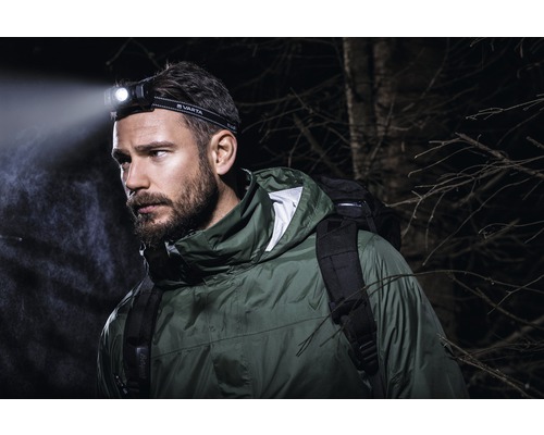 Bărbat cu lanternă frontală Varta și rucsac afară