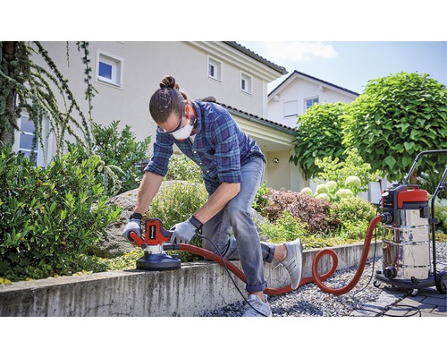 Un bărbat șlefuiește un zid de beton afară cu o șlefuitoare de beton și un aspirator.