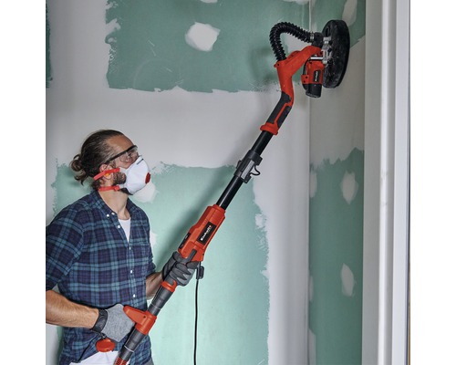 Un bărbat șlefuiește un perete cu o mașină de șlefuit gips-carton Einhell