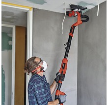 Un bărbat șlefuiește un tavan cu o șlefuitoare pentru gips-carton într-o cameră.