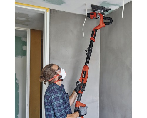 Un bărbat șlefuiește un tavan cu o șlefuitoare pentru gips-carton într-o cameră.