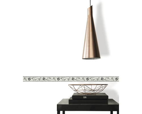 Bordură decorativă cu motiv floral pe un perete alb, combinată cu o lampă suspendată și o măsuță laterală.