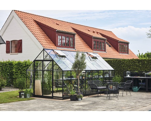 Seră cu pereți de sticlă și cadru negru în grădină cu mobilier de grădină