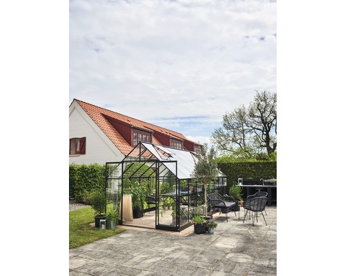 Seră cu plante și mobilier de grădină pe o terasă în fața unei case.