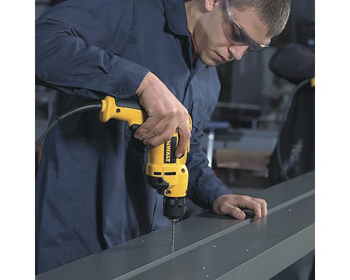 Un bărbat găurește un profil metalic cu o mașină de găurit galbenă.