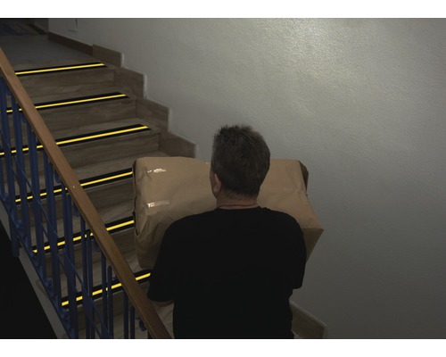 Bărbat care duce un pachet pe scări cu benzi antiderapante