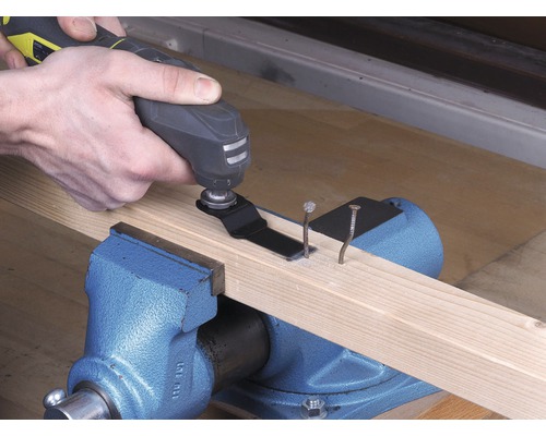 O persoană folosește un instrument multifuncțional pentru a tăia cuie într-o scândură de lemn, care este fixată într-o menghină.