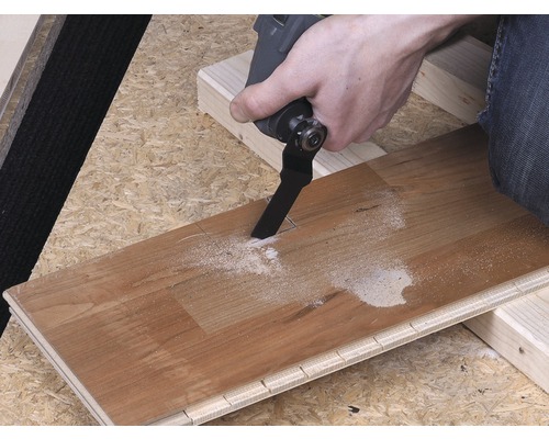 O persoană taie o scândură de lemn cu o unealtă multifuncțională.