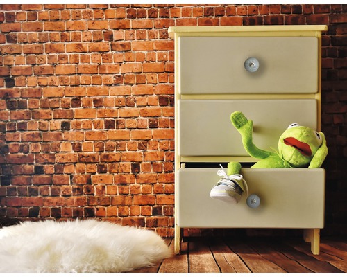 Comodă cu trei sertare, o păpușă de pluș și un pantof în fața unui perete de cărămidă