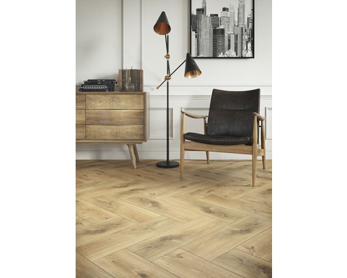 Living luminos cu parchet herringbone, dulap, lampă de podea și fotoliu.