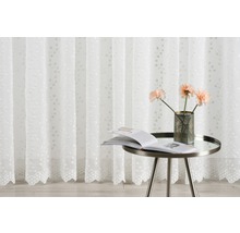 Perdea decorativă albă cu model floral, completată de o măsuță laterală cu o carte și o vază cu flori.
