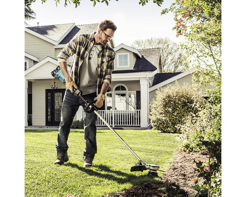 Un bărbat tunde gazonul cu o mașină de tuns iarba cu acumulator în grădina din fața unei case.