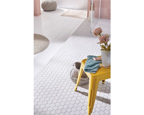 Baie cu gresie hexagonală albă, taburet galben, prosop și accesorii de baie.