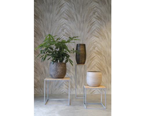 Scenă decorativă cu plantă de interior, jardinieră înaltă și jardinieră joasă pe taburete în fața unui perete cu model