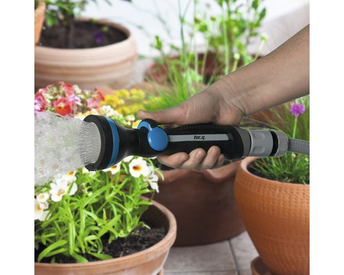 O mână ține un pistol de pulverizare pentru grădină for.q și udă plantele.