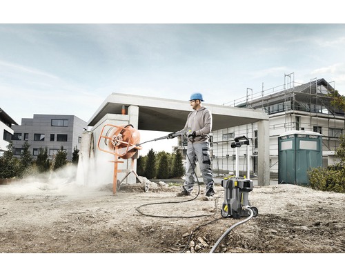 Un bărbat curăță un mixer de beton cu un curățător cu presiune înaltă pe un șantier.