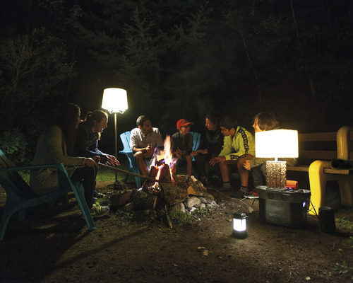 Un grup de oameni stă noaptea în jurul unui foc de tabără cu lămpi și o centrală electrică portabilă.