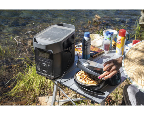 Scenă în aer liber cu o sursă portabilă de energie, un aparat de făcut vafe și ingrediente pentru micul dejun pe o masă.