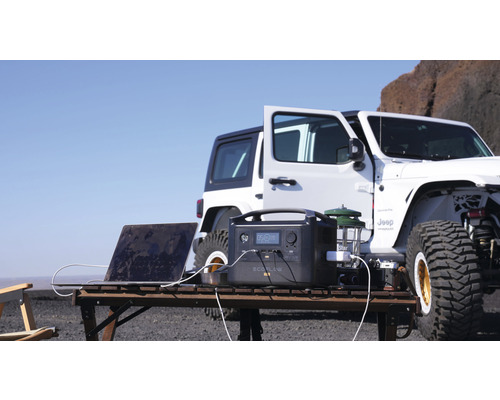 Centrală electrică portabilă cu laptop și lampă pe o masă în aer liber, cu o mașină în fundal