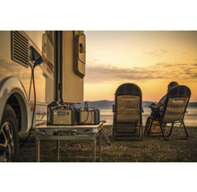 Scenă cu autorulotă, două centrale electrice portabile pe o masă și două scaune de camping pe malul lacului la apus.