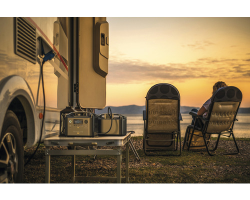 Scenă cu autorulotă, două centrale electrice portabile pe o masă și două scaune de camping pe malul lacului la apus.