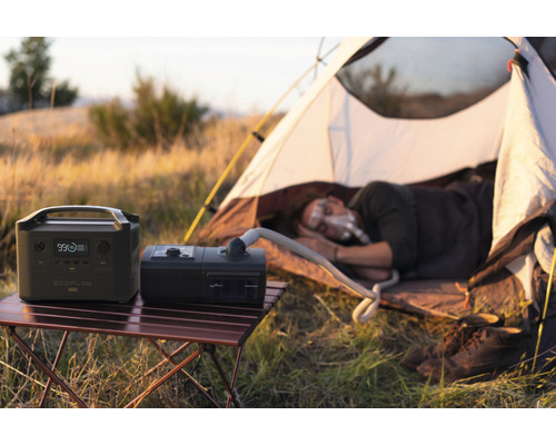 Scenă de camping cu centrală electrică portabilă, aparat CPAP și persoană care doarme