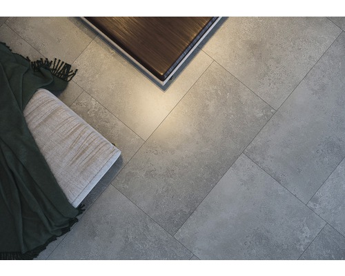 Prim-plan cu plăci de pardoseală gri, montate în model herringbone, cu o bancă și o masă