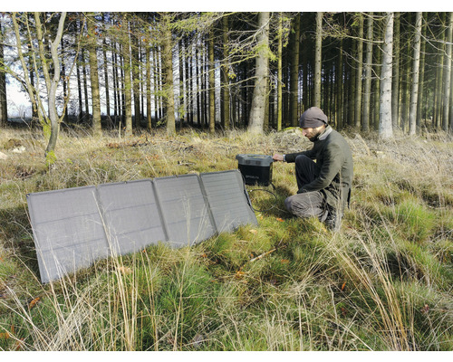 Un bărbat ghemuit în pădure manevrează un modul solar pentru a încărca un generator