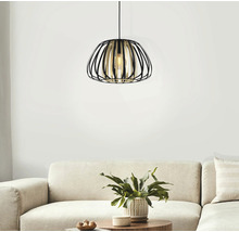 Lampa suspendată metalică cu design deschis, în formă de cușcă, deasupra unei canapele și a unei măsuțe de cafea cu o plantă.