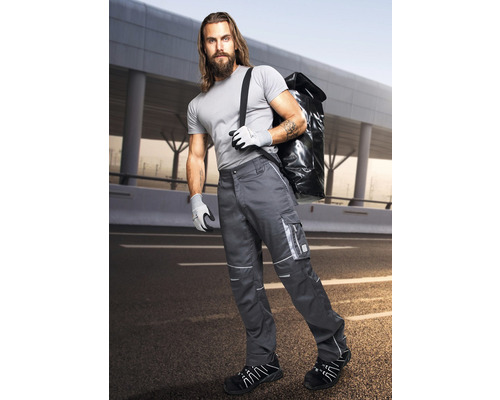 Bărbat în pantaloni de lucru cu buzunare laterale, mănuși de lucru și pantofi de lucru care poartă o geantă pe umăr